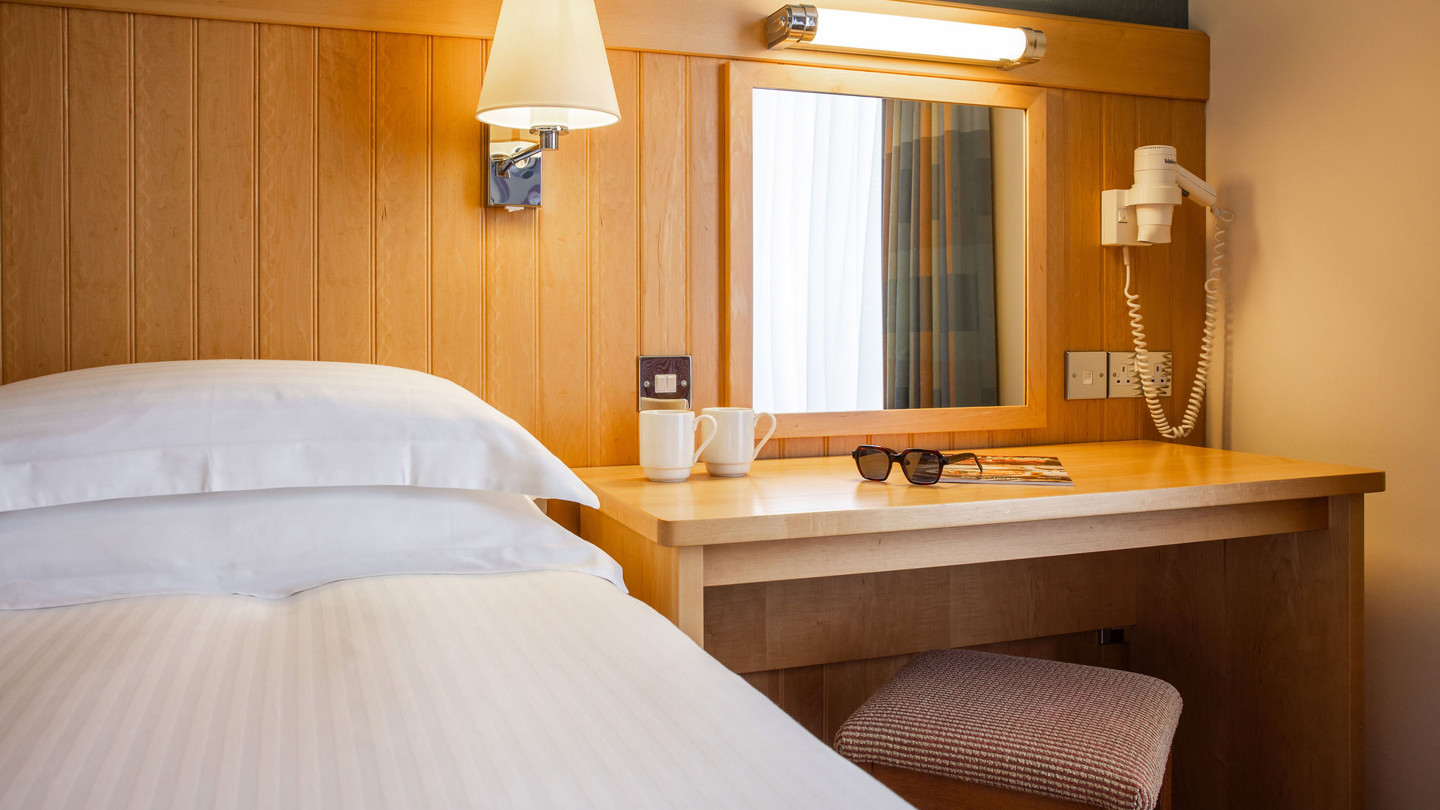 Bed with crisp white linen and a desk next to it.