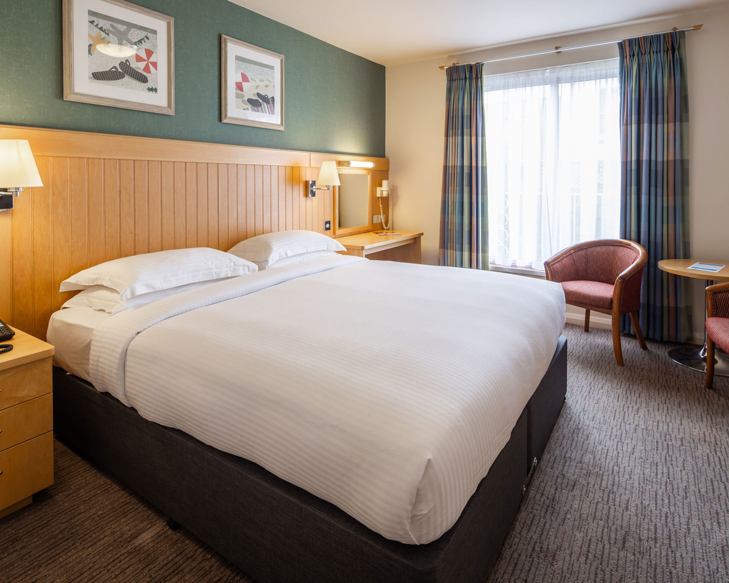 Double twin bed room with crisply made bed, desk and small round table with two armchairs.