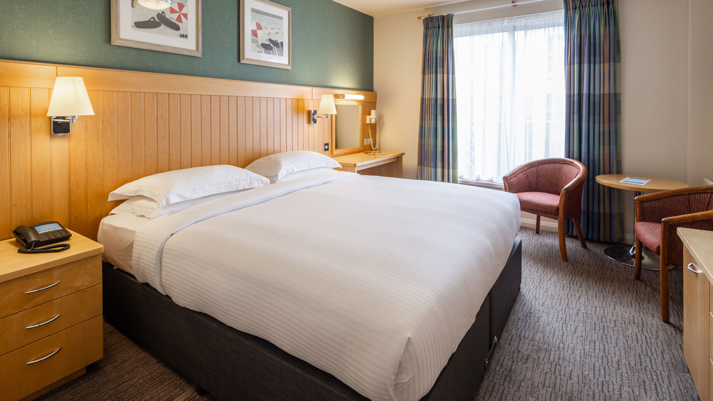 Double twin bed room with crisply made bed, desk and small round table with two armchairs.