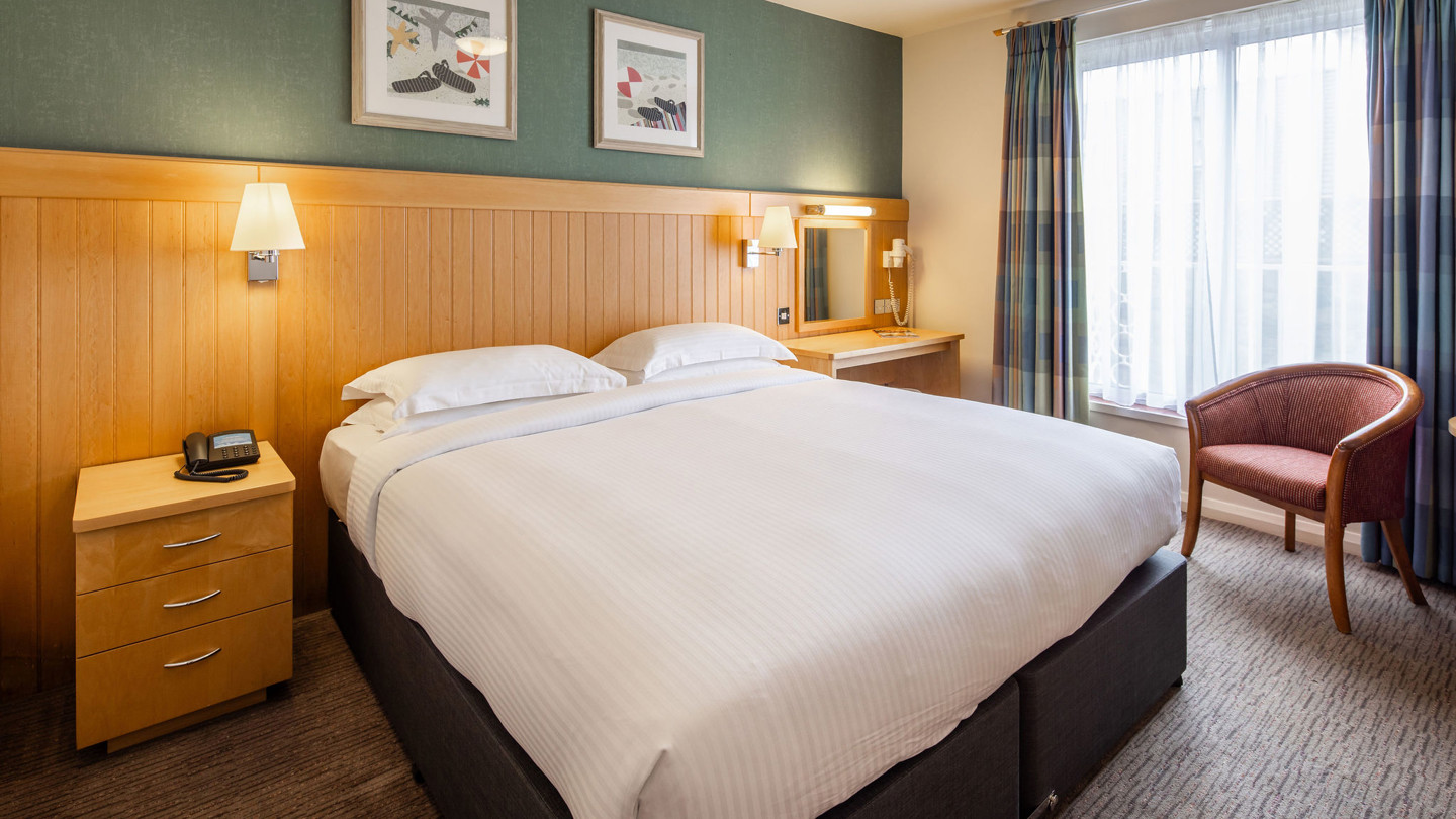 Double twin bed room with crisply made bed, desk and armchair.